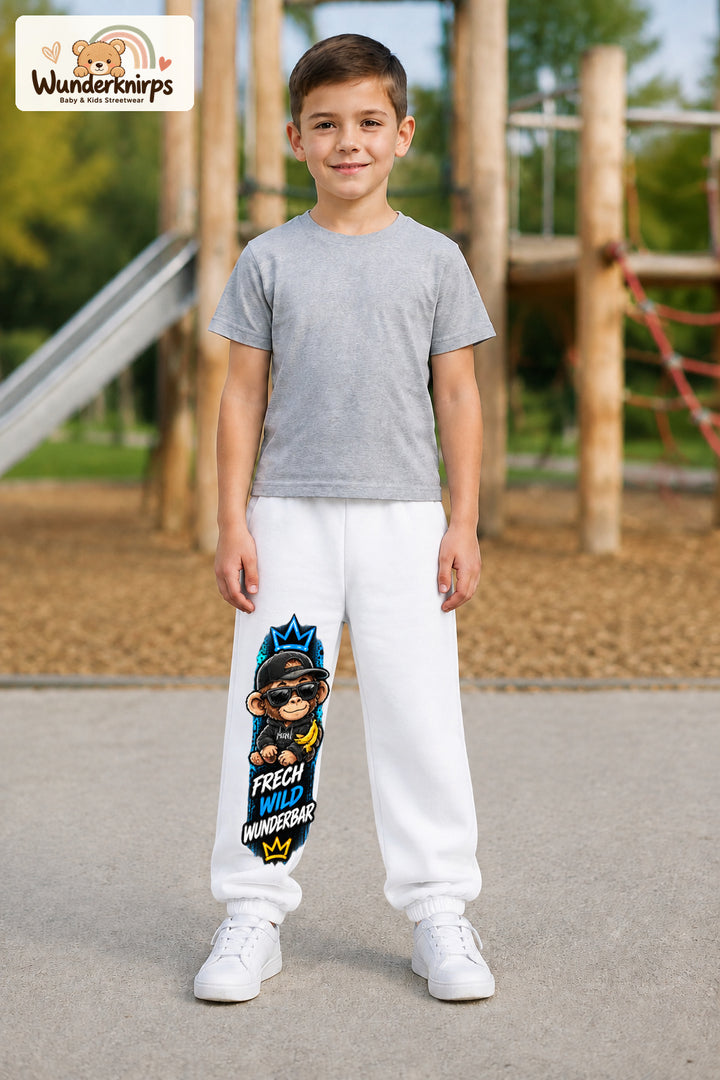 Junge trägt weiße Jogginghose mit Frech wild Affe-Print, von vorn auf dem Spielplatz.