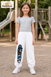 Mädchen trägt weiße Jogginghose mit Chill Play Affe-Print, von vorn auf dem Spielplatz.