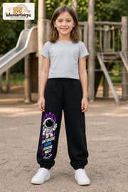 Mädchen trägt schwarze Jogginghose mit Eigene Welt Astronaut-Print, von vorn auf dem Spielplatz.