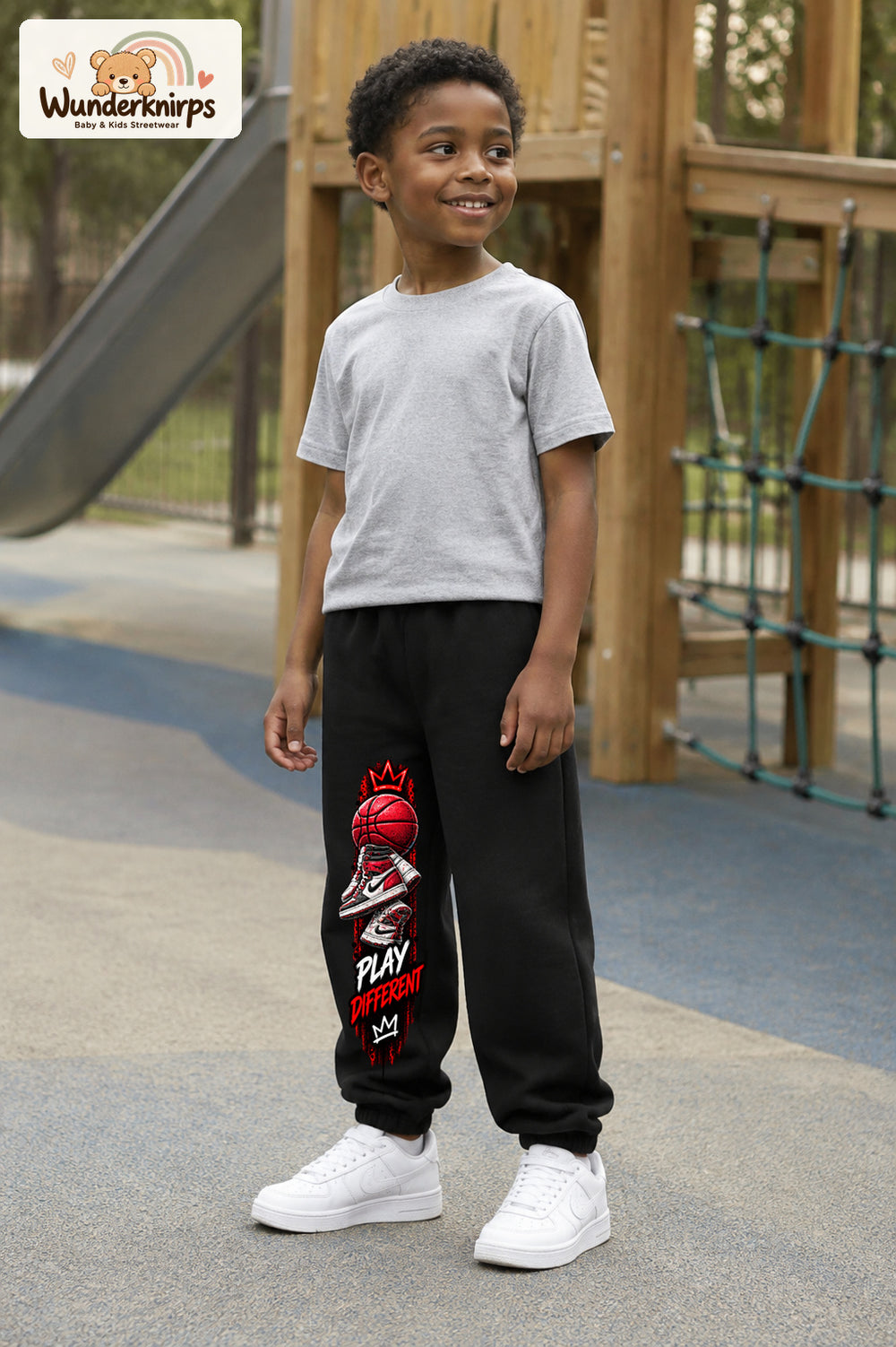 Junge trägt schwarze Jogginghose mit Play Different Basketball-Print, leicht seitlich auf dem Spielplatz.