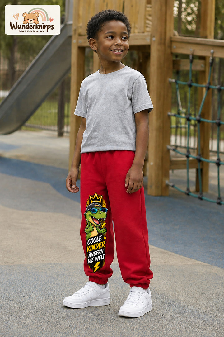 Junge trägt rote Jogginghose mit Coole Kinder Sonnenbrillen-Dino-Print, leicht seitlich auf dem Spielplatz.