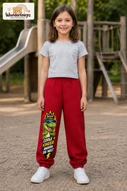 Mädchen trägt rote Jogginghose mit Coole Kinder Sonnenbrillen-Dino-Print, von vorn auf dem Spielplatz.