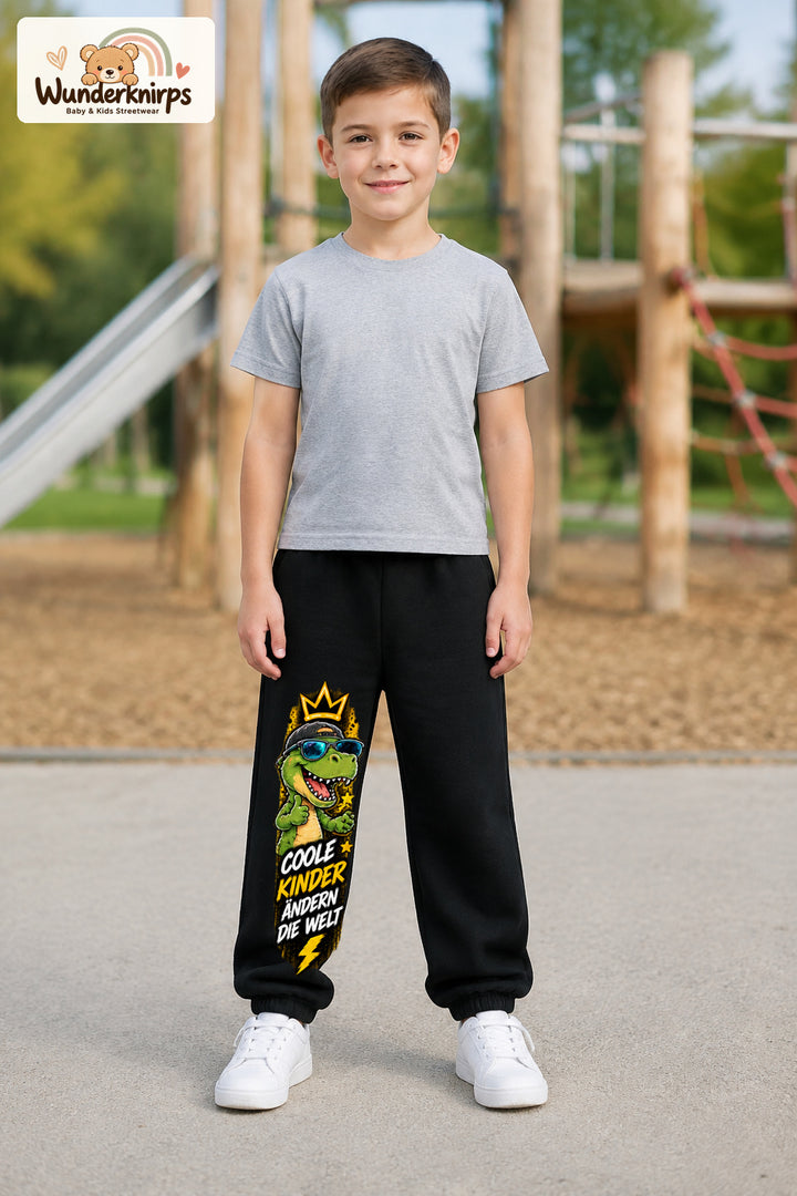 Junge trägt schwarze Jogginghose mit Coole Kinder Sonnenbrillen-Dino-Print, von vorn auf dem Spielplatz.