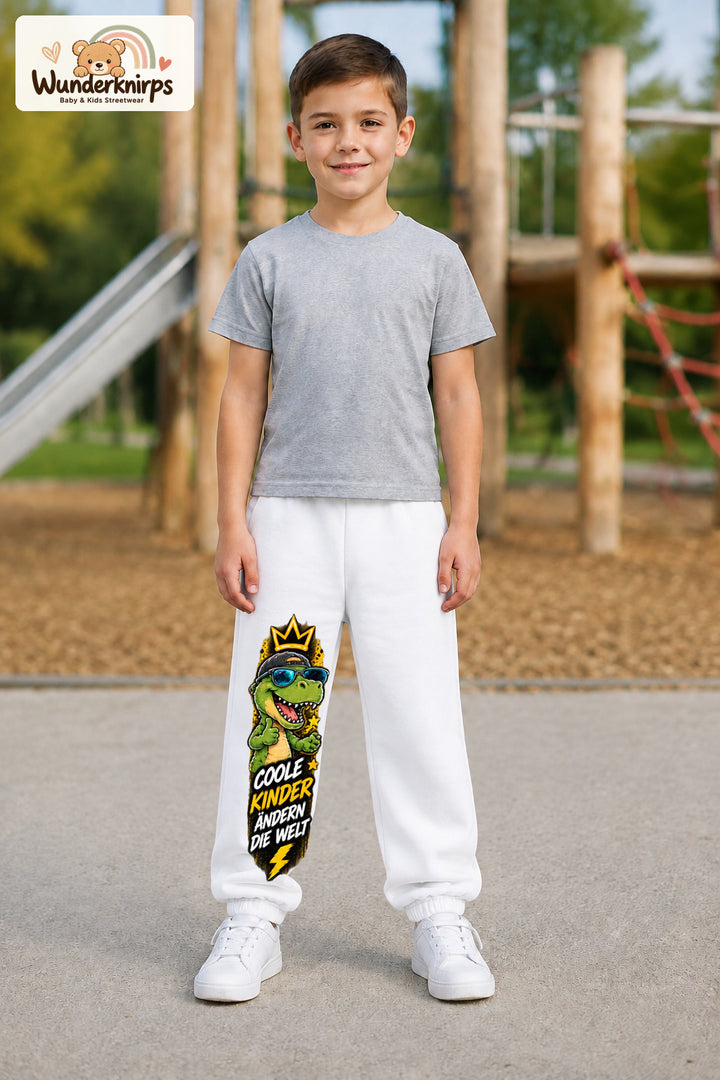 Junge trägt weiße Jogginghose mit Coole Kinder Sonnenbrillen-Dino-Print, von vorn auf dem Spielplatz.