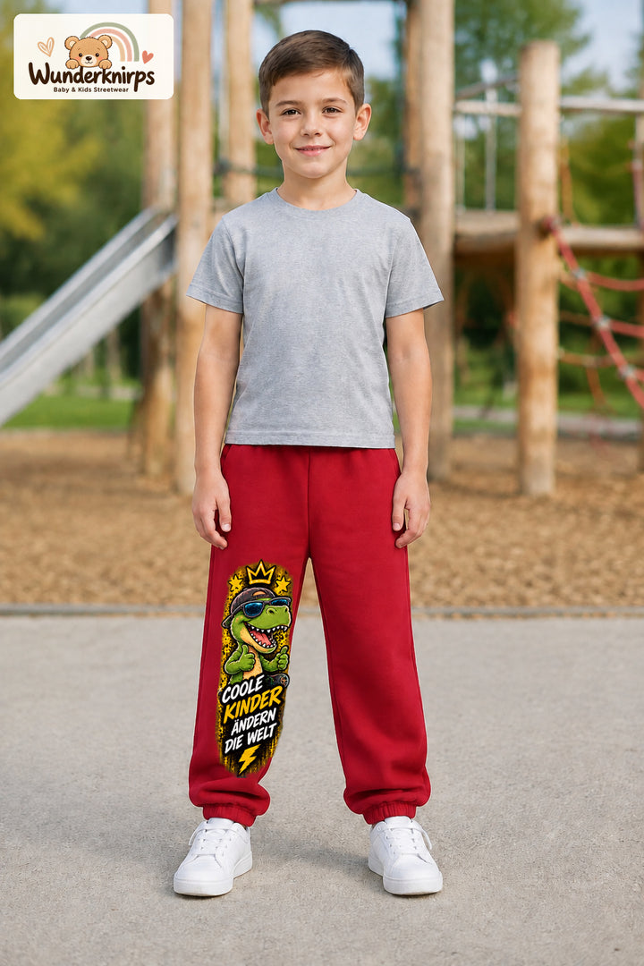 Junge trägt rote Jogginghose mit Coole Kinder Daumen-Dino-Print, von vorn auf dem Spielplatz.
