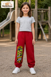 Mädchen trägt rote Jogginghose mit Coole Kinder Daumen-Dino-Print, von vorn auf dem Spielplatz.