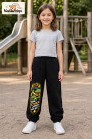 Mädchen trägt schwarze Jogginghose mit Coole Kinder Daumen-Dino-Print, von vorn auf dem Spielplatz.