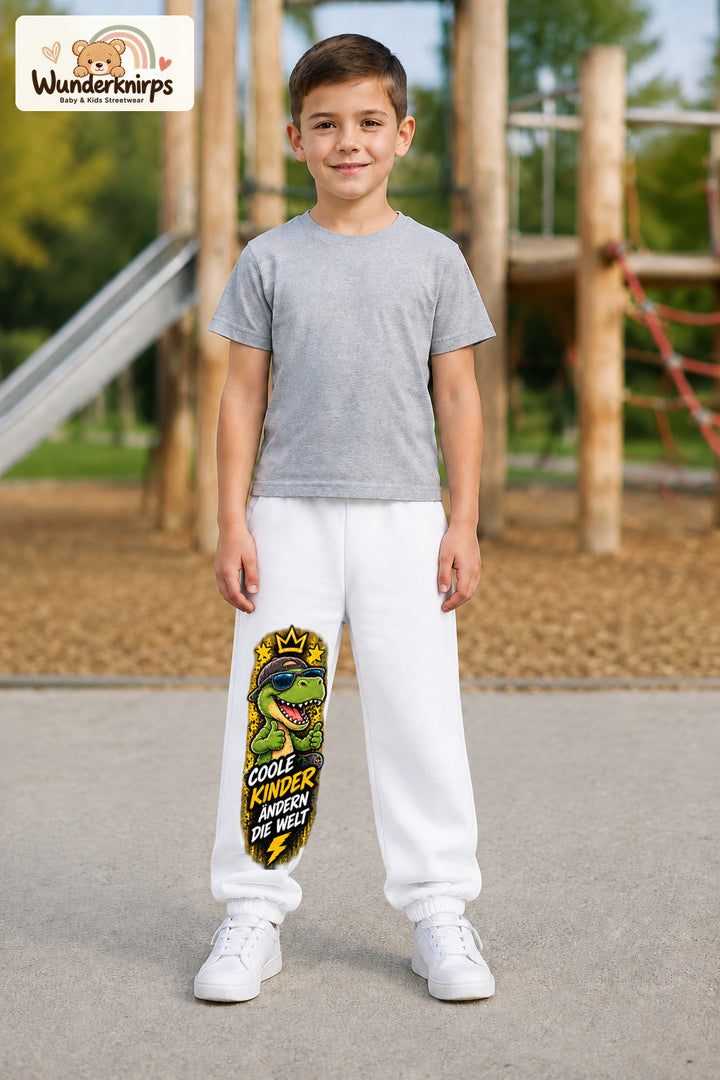 Junge trägt weiße Jogginghose mit Coole Kinder Daumen-Dino-Print, von vorn auf dem Spielplatz.