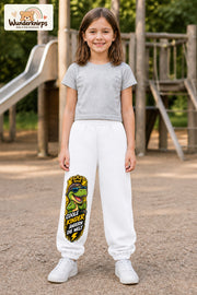 Mädchen trägt weiße Jogginghose mit Coole Kinder Daumen-Dino-Print, von vorn auf dem Spielplatz.