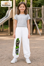 Mädchen trägt weiße Jogginghose mit Dino Crew T-Rex-Print, von vorn auf dem Spielplatz.