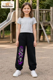 Mädchen trägt schwarze Jogginghose mit Strength Drache Violett-Print, von vorn auf dem Spielplatz.
