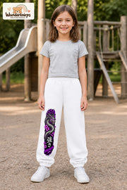 Mädchen trägt weiße Jogginghose mit Strength Drache Violett-Print, von vorn auf dem Spielplatz.