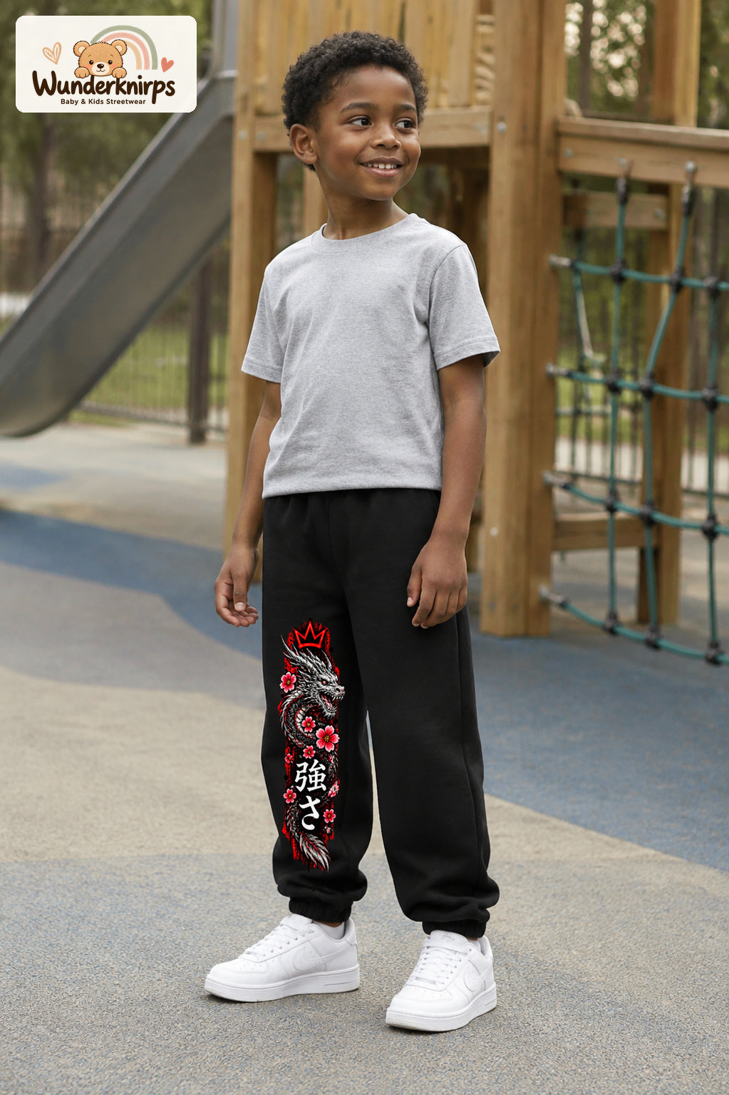 Junge trägt schwarze Jogginghose mit Roter Blütendrache-Print, leicht seitlich auf dem Spielplatz.