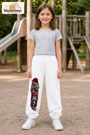 Mädchen trägt weiße Jogginghose mit Roter Blütendrache-Print, von vorn auf dem Spielplatz.