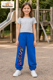 Mädchen trägt blaue Jogginghose mit Blütendrache Lila-Print, von vorn auf dem Spielplatz.
