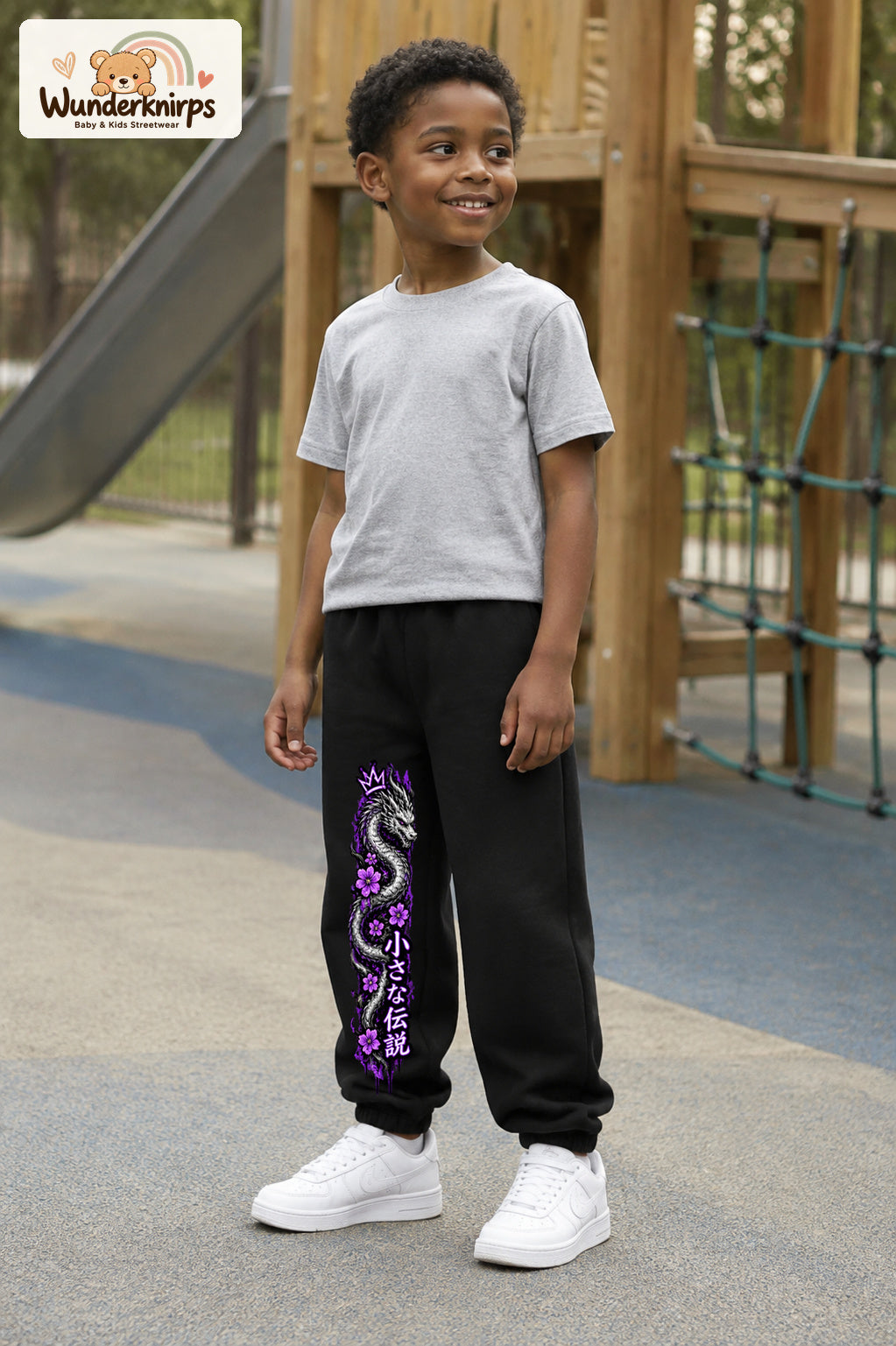 Junge trägt schwarze Jogginghose mit Blütendrache Lila-Print, leicht seitlich auf dem Spielplatz.