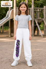 Mädchen trägt weiße Jogginghose mit Blütendrache Lila-Print, von vorn auf dem Spielplatz.