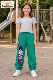 Mädchen trägt grüne Jogginghose mit Alles möglich Einhorn-Print, von vorn auf dem Spielplatz.