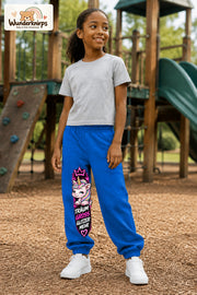Mädchen trägt blaue Jogginghose mit Träum groß Einhorn-Print, leicht seitlich auf dem Spielplatz.