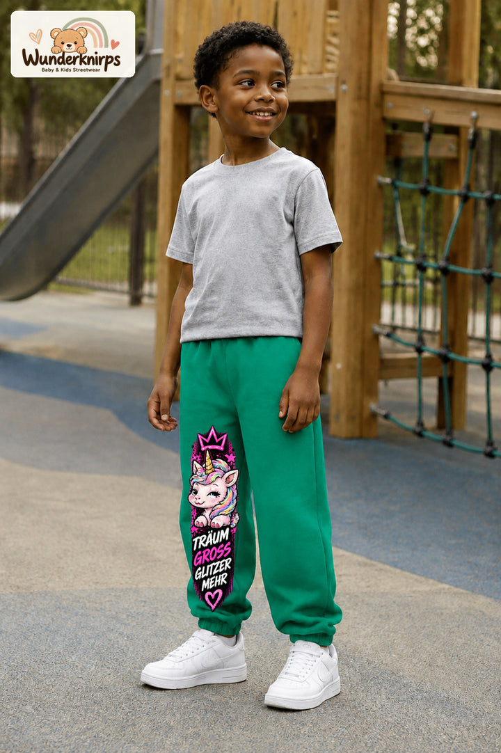 Junge trägt grüne Jogginghose mit Träum groß Einhorn-Print, leicht seitlich auf dem Spielplatz.