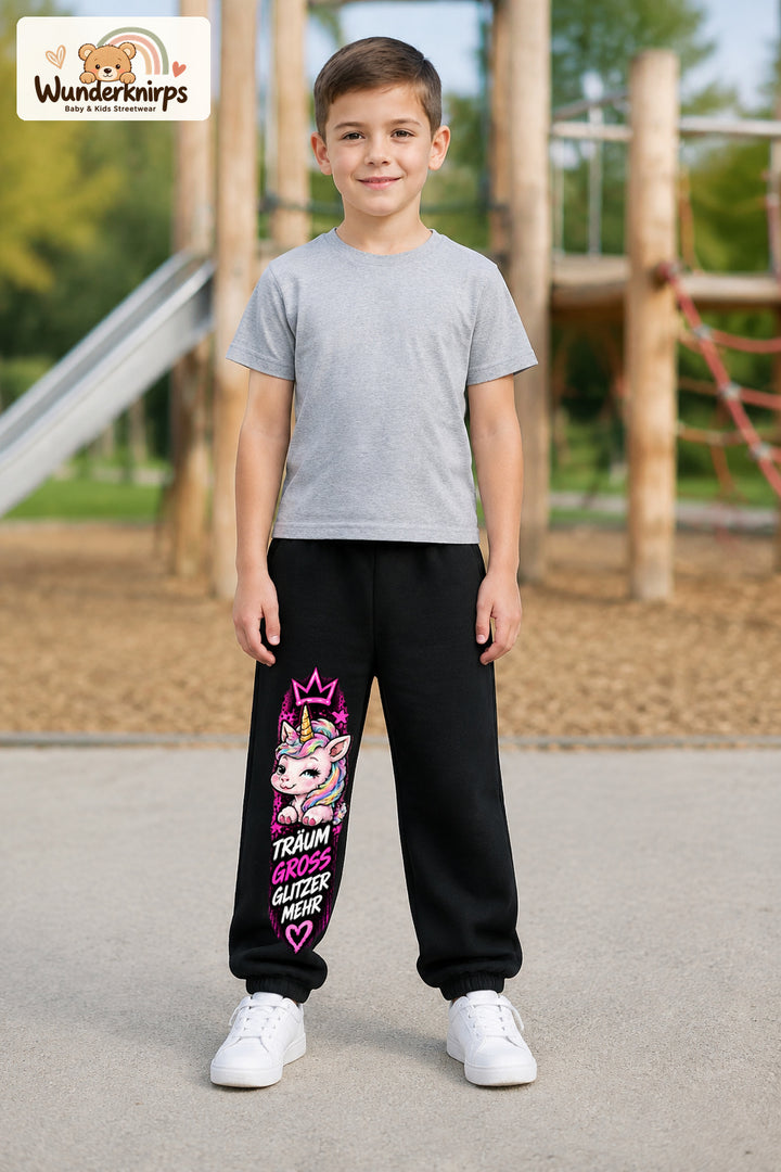 Junge trägt schwarze Jogginghose mit Träum groß Einhorn-Print, von vorn auf dem Spielplatz.