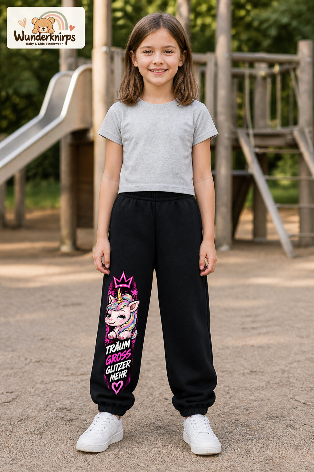 Mädchen trägt schwarze Jogginghose mit Träum groß Einhorn-Print, von vorn auf dem Spielplatz.
