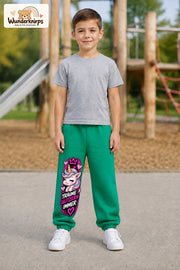 Junge trägt grüne Jogginghose mit Träume glitzern Einhorn-Print, von vorn auf dem Spielplatz.