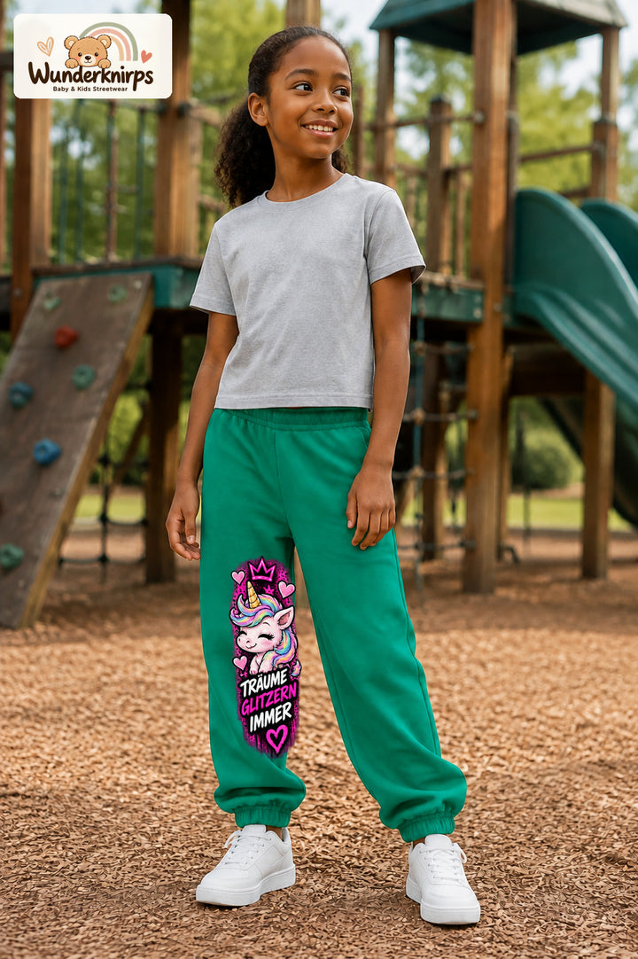 Mädchen trägt grüne Jogginghose mit Träume glitzern Einhorn-Print, leicht seitlich auf dem Spielplatz.