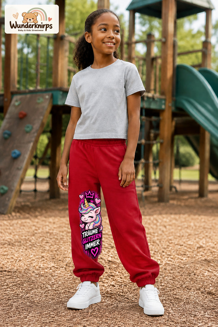 Mädchen trägt rote Jogginghose mit Träume glitzern Einhorn-Print, leicht seitlich auf dem Spielplatz.