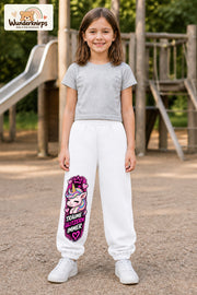 Mädchen trägt weiße Jogginghose mit Träume glitzern Einhorn-Print, von vorn auf dem Spielplatz.