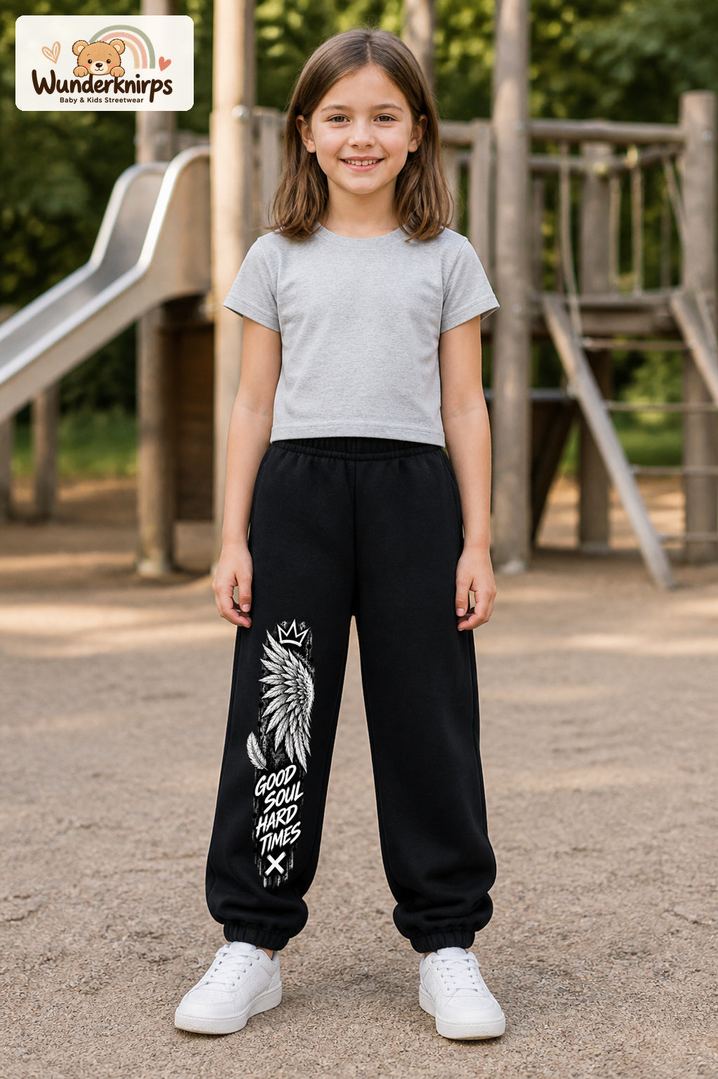 Mädchen trägt schwarze Jogginghose mit Good Soul Flügel-Print, von vorn auf dem Spielplatz.