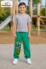 Junge trägt grüne Jogginghose mit Bessere Zukunft Erde-Print, von vorn auf dem Spielplatz.