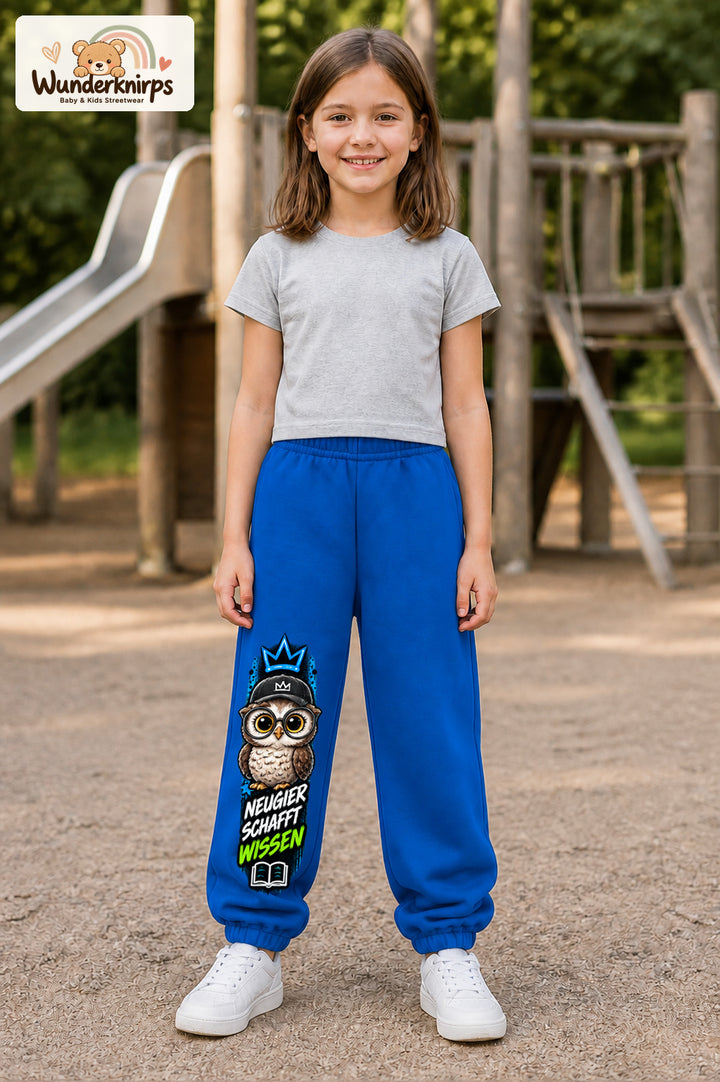 Mädchen trägt blaue Jogginghose mit Neugier Eule-Print, von vorn auf dem Spielplatz.