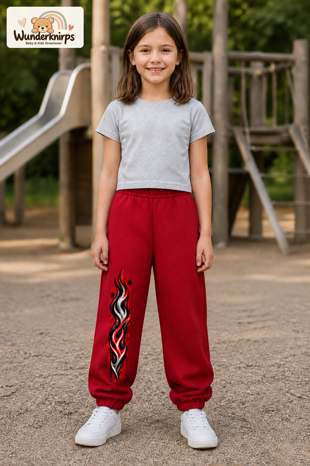 Mädchen trägt rote Jogginghose mit Rote Flammen-Print, von vorn auf dem Spielplatz.