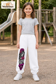 Mädchen trägt weiße Jogginghose mit Schönheit ohne Perfektion-Print, von vorn auf dem Spielplatz.