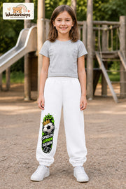 Mädchen trägt weiße Jogginghose mit Spielen Lernen Fußball-Print, von vorn auf dem Spielplatz.