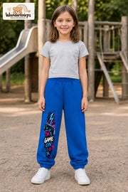 Mädchen trägt blaue Jogginghose mit Game On Controller-Print, von vorn auf dem Spielplatz.