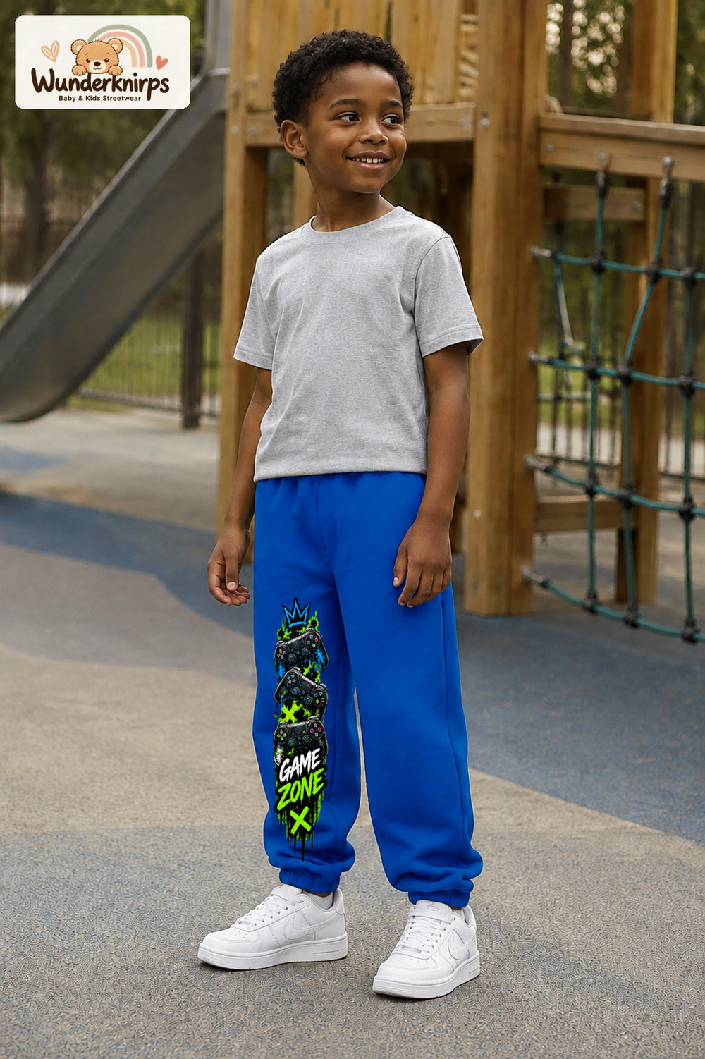 Junge trägt blaue Jogginghose mit Game Zone Controller-Print, leicht seitlich auf dem Spielplatz.