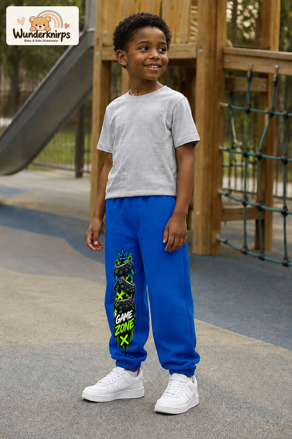 Junge trägt blaue Jogginghose mit Game Zone Controller-Print, leicht seitlich auf dem Spielplatz.