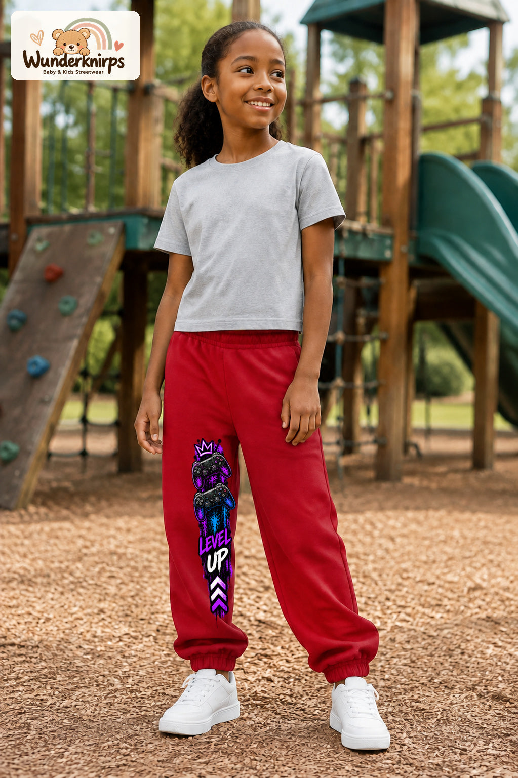 Mädchen trägt rote Jogginghose mit Level Up Gaming-Print, leicht seitlich auf dem Spielplatz.