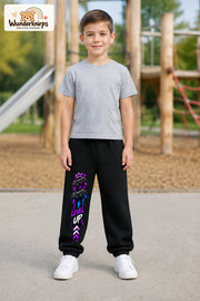 Junge trägt schwarze Jogginghose mit Level Up Gaming-Print, von vorn auf dem Spielplatz.