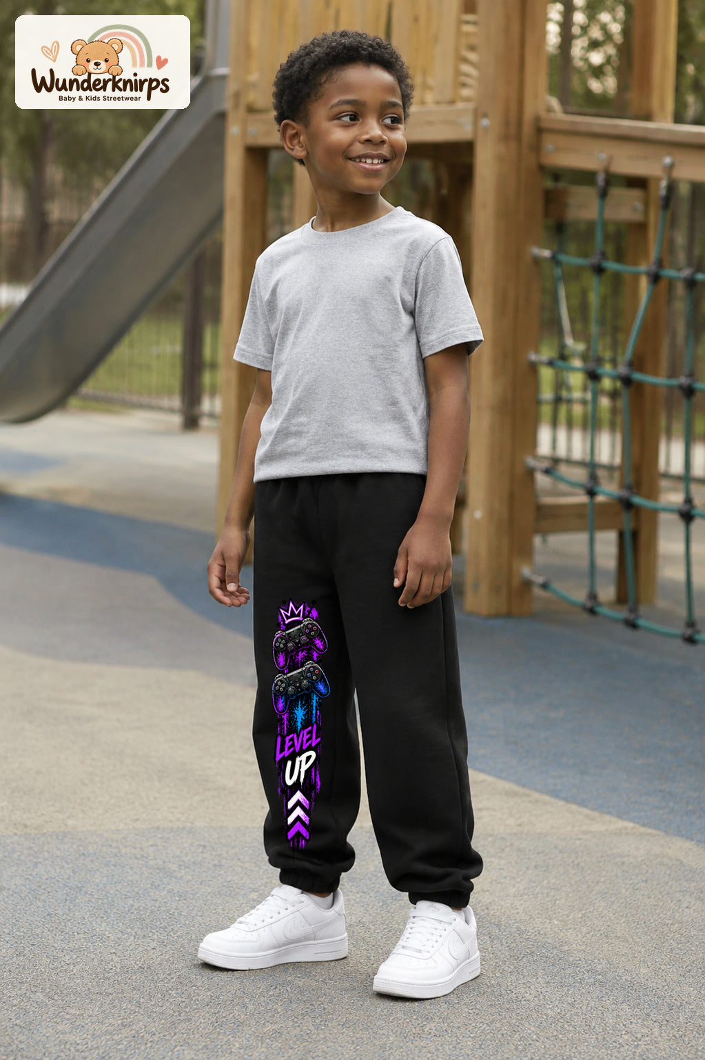 Junge trägt schwarze Jogginghose mit Level Up Gaming-Print, leicht seitlich auf dem Spielplatz.