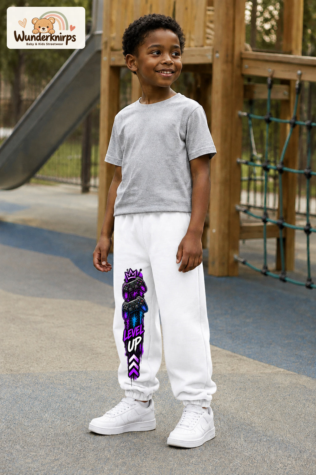 Junge trägt weiße Jogginghose mit Level Up Gaming-Print, leicht seitlich auf dem Spielplatz.