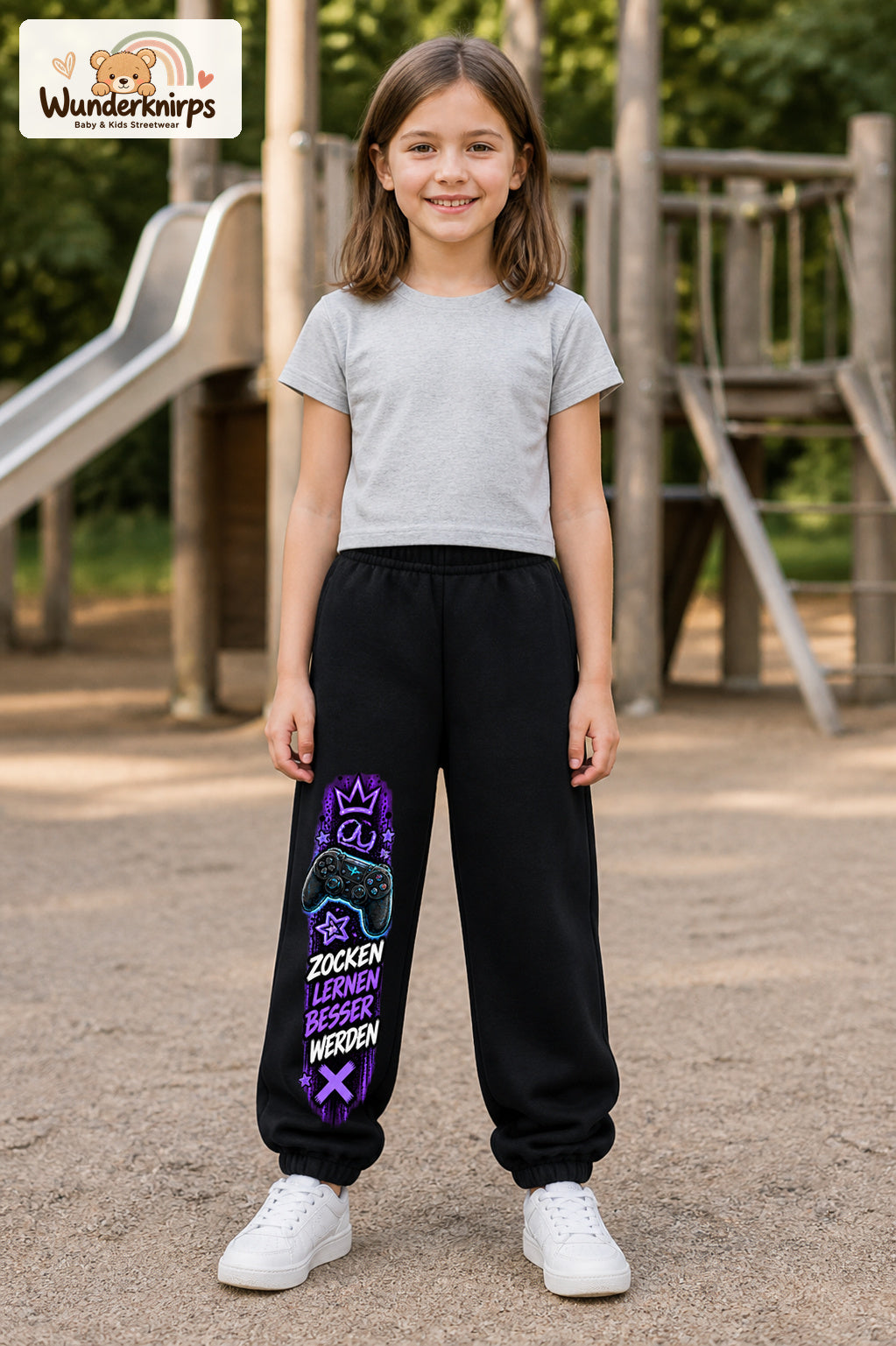 Mädchen trägt schwarze Jogginghose mit Zocken Lernen Controller-Print, von vorn auf dem Spielplatz.