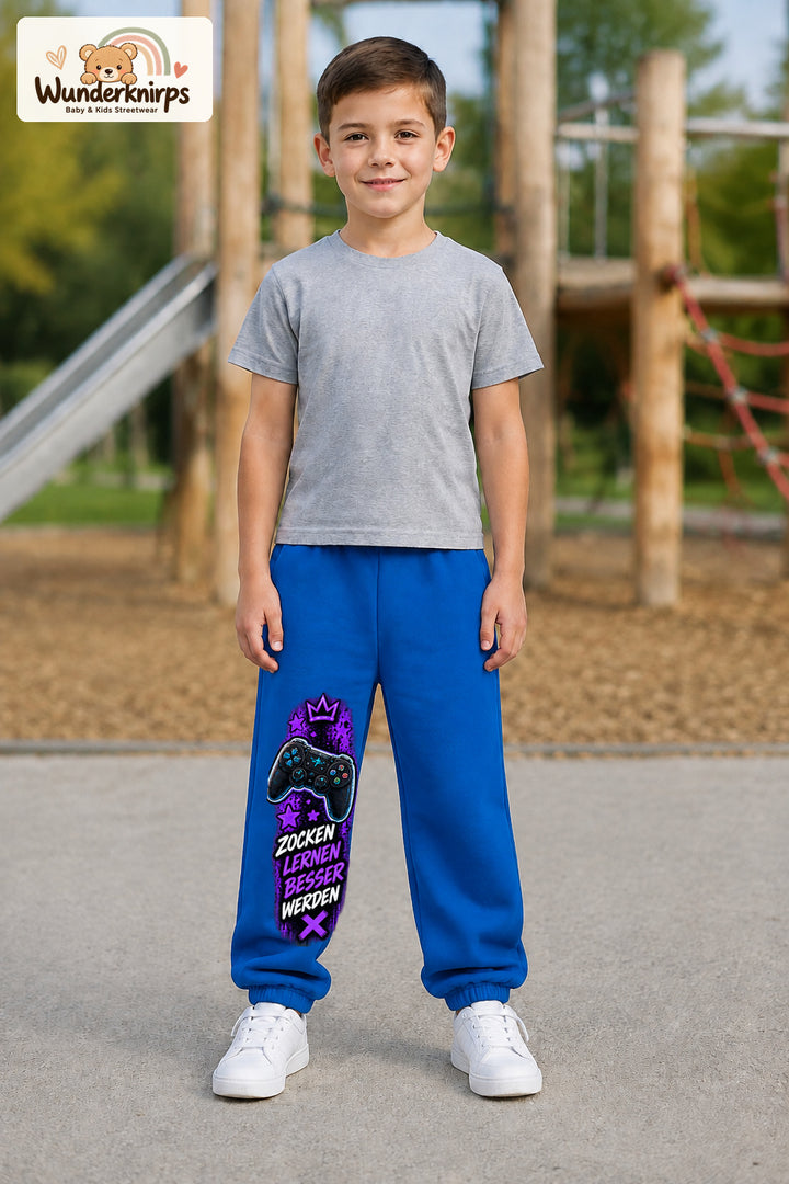 Junge trägt blaue Jogginghose mit Gaming Sterne Violett-Print, von vorn auf dem Spielplatz.