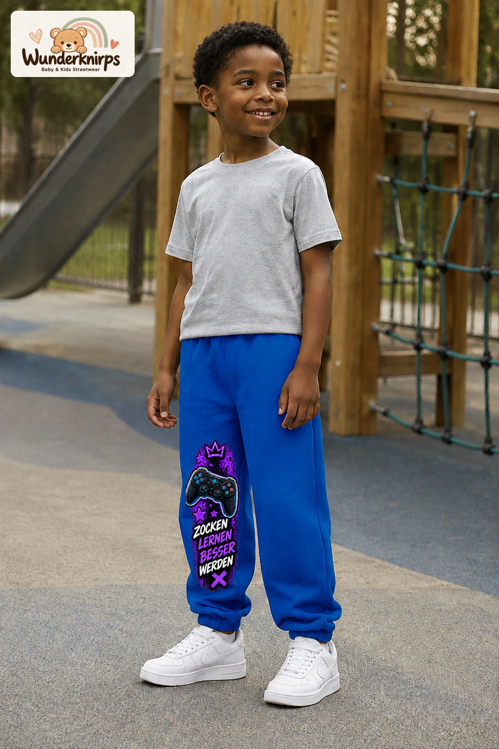 Junge trägt blaue Jogginghose mit Gaming Sterne Violett-Print, leicht seitlich auf dem Spielplatz.