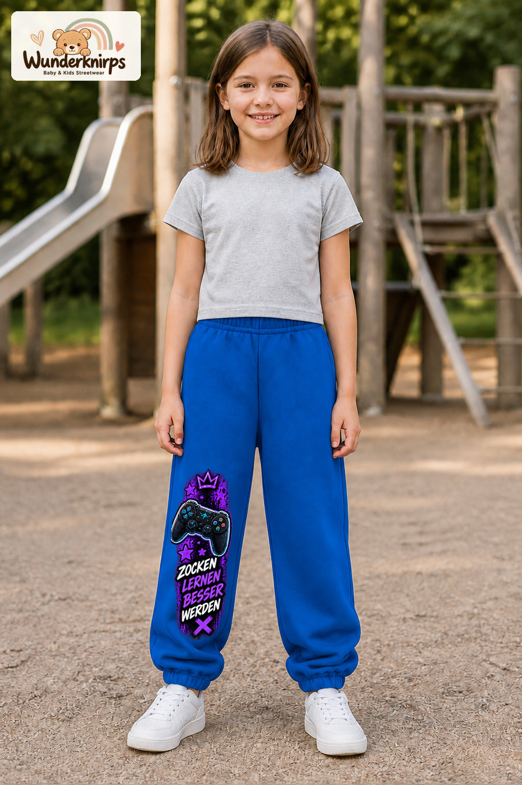 Mädchen trägt blaue Jogginghose mit Gaming Sterne Violett-Print, von vorn auf dem Spielplatz.