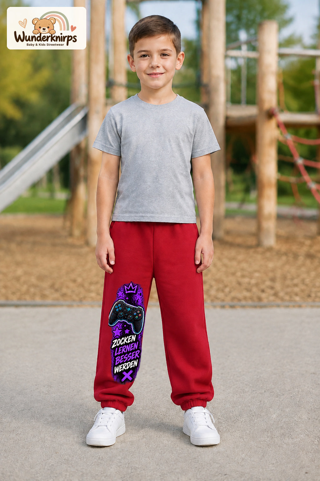Junge trägt rote Jogginghose mit Gaming Sterne Violett-Print, von vorn auf dem Spielplatz.