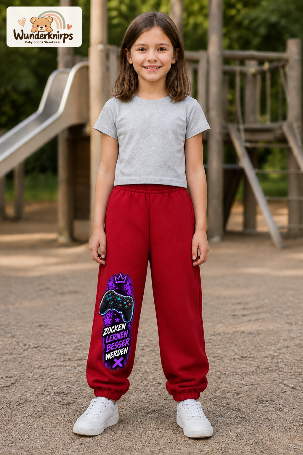Mädchen trägt rote Jogginghose mit Gaming Sterne Violett-Print, von vorn auf dem Spielplatz.