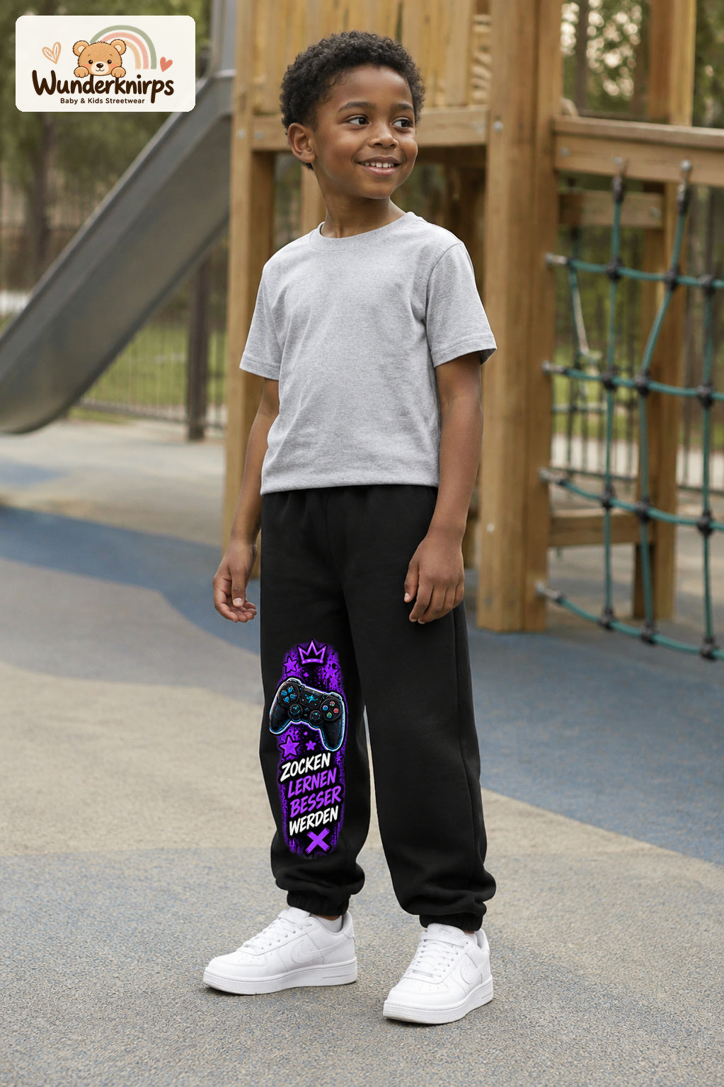 Junge trägt schwarze Jogginghose mit Gaming Sterne Violett-Print, leicht seitlich auf dem Spielplatz.